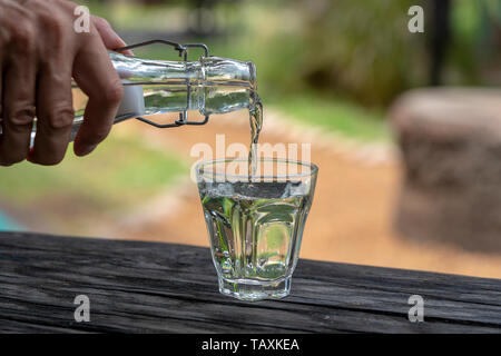 A waiter in a restaurant pours fresh water from a bottle into a glass, close up, outdoors Stock Photo