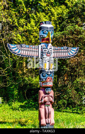 The colorful 'Thunderbird House Post Totem Pole' that has a Thunderbird at the top, then below that a Grizzly bear holding a human in Stanley park, BC Stock Photo