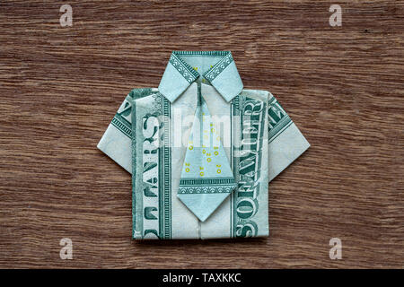 Origami shirt made of dollar banknote on wooden background. Close up. Dollar bill T-shirt Stock Photo