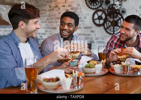 Friends Eating Burgers And Enjoying Beer, Sitting In Bar Stock Photo