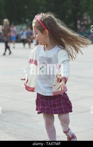 Little happy girl playing with the soap bubbles in the center of town. Child running around and catching the soap bubbles. Candid people, real moments Stock Photo