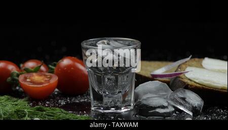 Shot of vodka in glass. Bread with lard, onion, dill and cherry tomatoes against black background Stock Photo