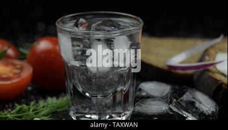Shot of vodka in glass. Bread with lard, onion, dill and cherry tomatoes against black background Stock Photo