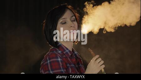 Beautiful, young woman smoking hookah. Attractive girl smoking flavored tobacco. Blow out smoke on black background Stock Photo