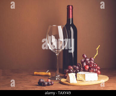 A bottle of wine an empty glass bunch of red grapes a slice of cheese on a dark background. Copy space. Selective focus.