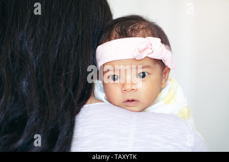 Closeup portrait of cute adorable awake Asian Chinese mixed race newborn baby girl with open eyes lying on parent shoulder. Healthy happy childhood et Stock Photo
