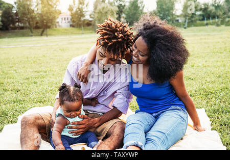 Happy African family spending time together during the weekend outdoor - Black mother and father having fun with their daughter in a public park