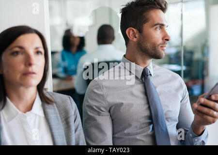 Young man using his cellphone and looking deep in thought while sitting with another job applicant waiting for his interview Stock Photo