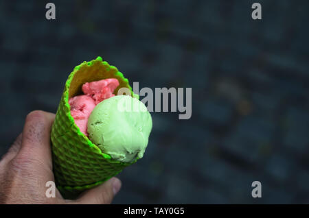 a man holding a green tube of strawberry and pistachio ice cream on a background of gray stone pavement.Close up,space for text Stock Photo
