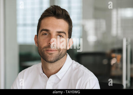 Portrait of a young businessman smiling confidently while sitting alone at his desk in a modern office Stock Photo