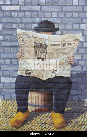 A man with a bowler hat (Derby), suit and wooden clogs reading a newspaper on a beautiful graffiti/wall painting in Zierikzee (Zeeland), Netherlands Stock Photo