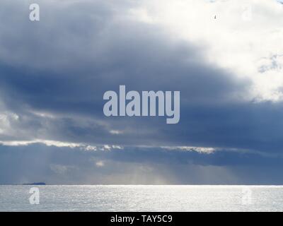 seascape in blue grey. Sunlight shining breaking through storm clouds, shimmering on the sea water, reflecting on Pacific ocean off Australian Coast Stock Photo
