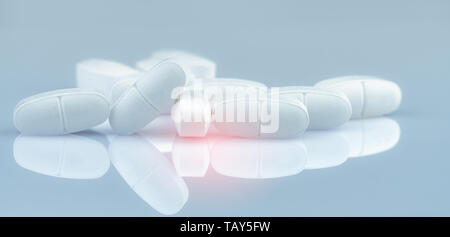 Pile of white oblong tablets pills on gradient background. White antibiotic tablet pills. Pharmaceutical industry. Pharmacy product. Drug in pharmacy  Stock Photo