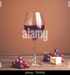 A glass of wine a bunch of red grape cheese slice dark background. Copy space. Still life style dark. Selective focus. Stock Photo