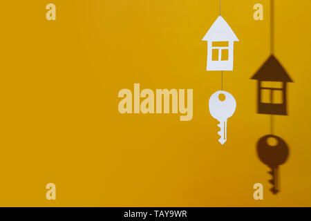 a small house and key made of cardboard casts a shadow on a bright colored background Stock Photo
