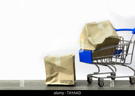 Bad delivery concepts. A damaged container box in small blue shopping cart model and on wood table with white background. Depicts transportation of go Stock Photo