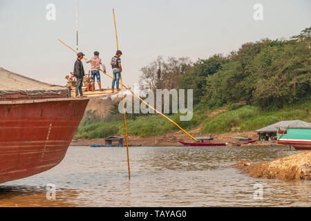 Nakaraj Nakhon, Laos - Feb 2016: Laotians pushing the ship with big poles over the Mekong river Stock Photo