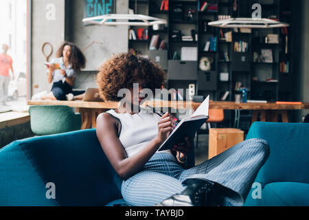 two young multiracial women writing and working in modern open space – freelance, interaction, communication Stock Photo