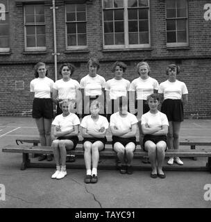 1950s, historical, teenage secondary schoolgirls posing for a picture in their PE kit - simple white t-shirt, black shorts and wearing plimsols, outside their inner-city school building, England, UK. Stock Photo