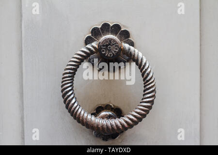 horizontal front view closeup on vintage rusted metallic door knob with knocking ring on white wooden background Stock Photo