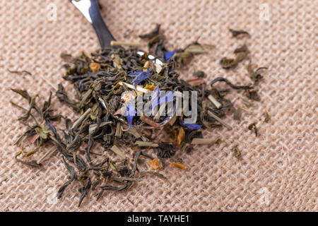 Dried leaves of herbal green tea with citrus peel and blue flowers on a sackcloth Stock Photo