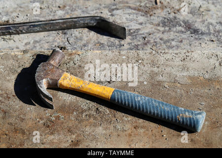 A closeup of a metal crowbar and a multicolored metal hammer on a concrete surface during a sunny spring day. Photographed in Madeira. Stock Photo