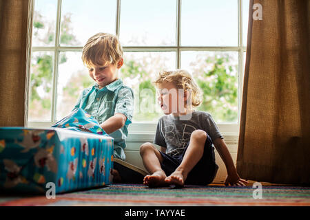 Young boy opening birthday presents while his brother watches. Stock Photo