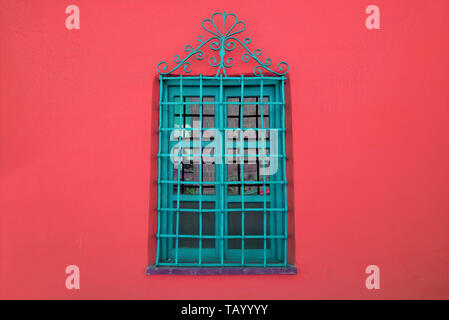 Turquoise blue wrought iron window on vibrant red concrete wall Stock Photo