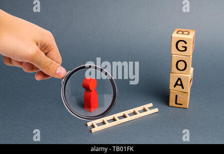 Magnifying glass is looking at a red figure of a man stands near fallen ladder and a tower of cubes with an inscription goal. achieving the goal, subj Stock Photo