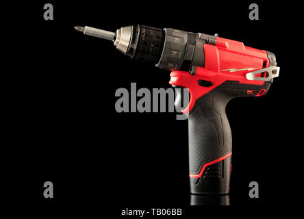 Cordless drill driver in red with rubberized handle in profile, isolated on black background with reflection Stock Photo