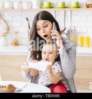 Business mom talking on phone and taking notes from baby hands