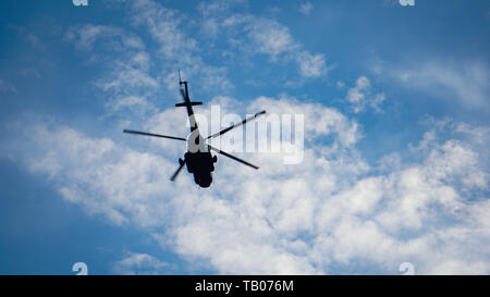 Silhouette of helicopter in blue white clouds sky. Stock Photo