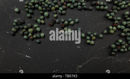 Top down view, Black pepper (Piper nigrum) spice spilled on dark working board. Turkish green / blue peppercorn variant. Stock Photo