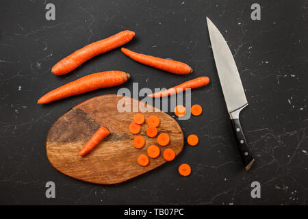 Top down view, chef knife, carrots, some of them sliced on chopping board. Stock Photo