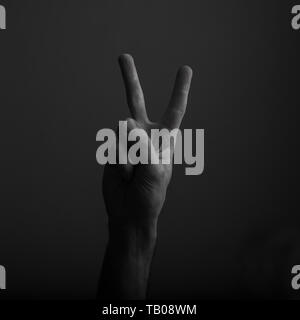 Male hand showing victory V hand sign against a dark background Stock Photo