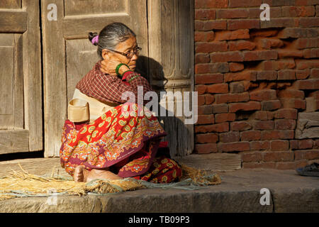 Elderly women (wearing back brace) sitting in sun on stoop of home in old town Dhulikhel, Nepal Stock Photo