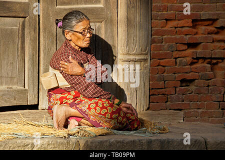 Elderly women (wearing back brace) sitting in sun on stoop of home in old town Dhulikhel, Nepal Stock Photo