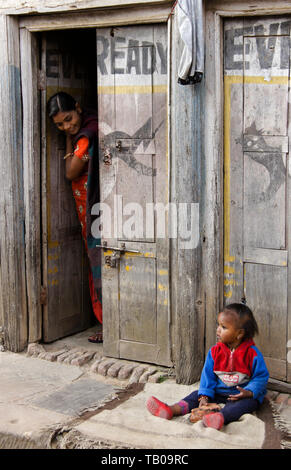 Mother checking on her young child sitting on stoop of home in old town Dhulikhel, Nepal Stock Photo