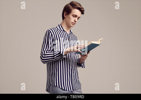 Fashion portrait of young handsome man in striped shirt reading a book on gray background in studio Stock Photo