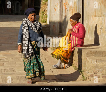 Elderly women in traditional dress walking on stone street and sitting in sun in old town Dhulikhel, Nepal Stock Photo
