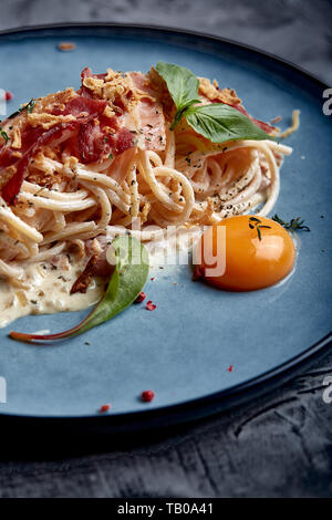 Classic pasta carbonara with yolk on a plate. Pasta laid out on a blue plate on a dark background. Concept of Italian cuisine, beautiful serving Stock Photo