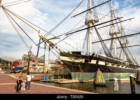 Baltimore, Maryland, USA - July 11, 2017: Two girls walk past the USS Constellation, one of the historic ships docked in Baltimore's Inner Harbor. Bui Stock Photo