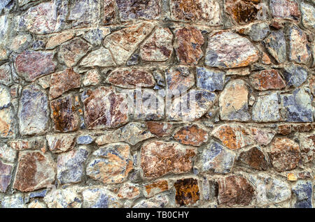 Multi-colored background of untreated natural stone, on the facade of the old oval tower of stones of different breeds and shades Stock Photo