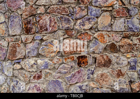 Motley background of stones of different breeds and shades of raw natural stone on the facade of the old oval tower Stock Photo