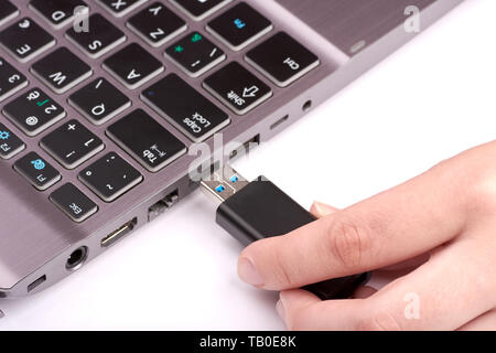 Closeup view of silver laptop. A woman holds a black flash drive or stick in her hand and connects it to a port or slot. Isolated on white background Stock Photo