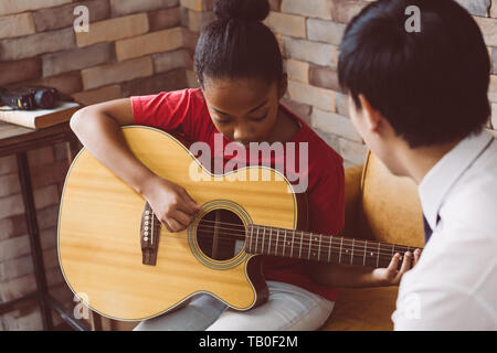African American girl in casual outfit learning how to play guitar while sitting on couch near male tutor during music lesson Stock Photo