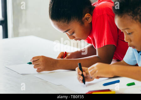 African American kids learning how to draw with crayon on table inside indoors room in natural ambient light Stock Photo