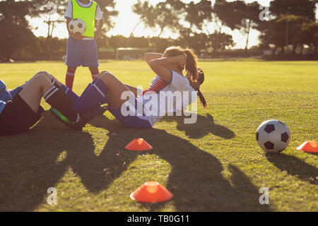 Determined female soccer players doing crunches on the field Stock Photo