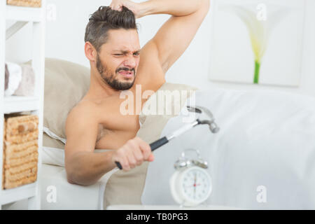man smashing alarm clock with hammer on bed Stock Photo