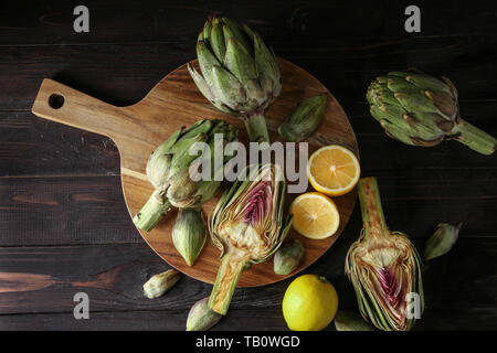 Wooden board with raw artichokes and lemons on table Stock Photo